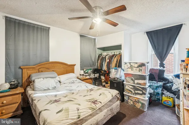 a bedroom with a bed a standing fan and a dresser