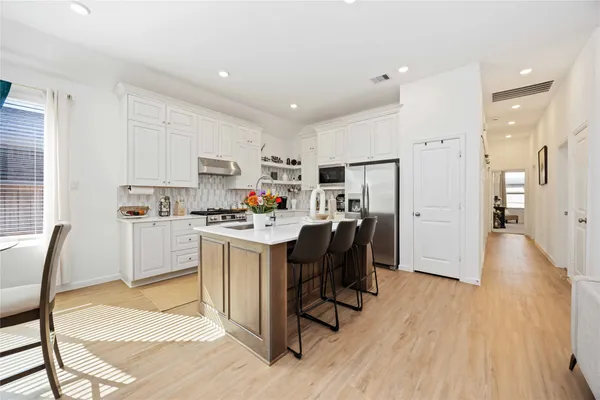 a kitchen with stainless steel appliances kitchen island granite countertop a refrigerator a stove a sink and white cabinets with wooden floor