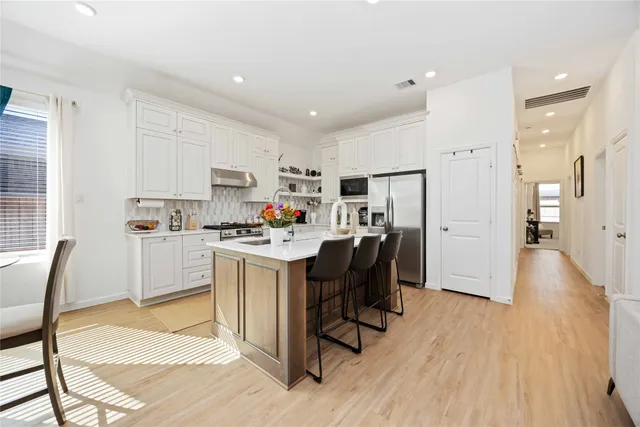 a kitchen with stainless steel appliances kitchen island granite countertop a refrigerator a stove a sink and white cabinets with wooden floor