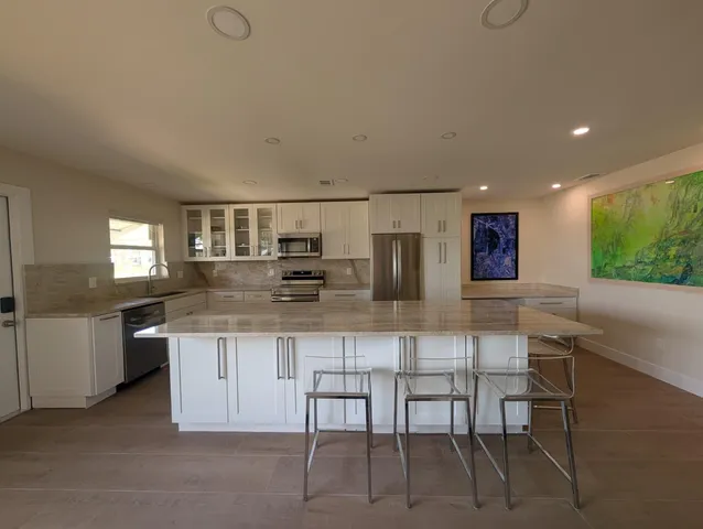 a kitchen with stainless steel appliances kitchen island granite countertop a table chairs sink and cabinets