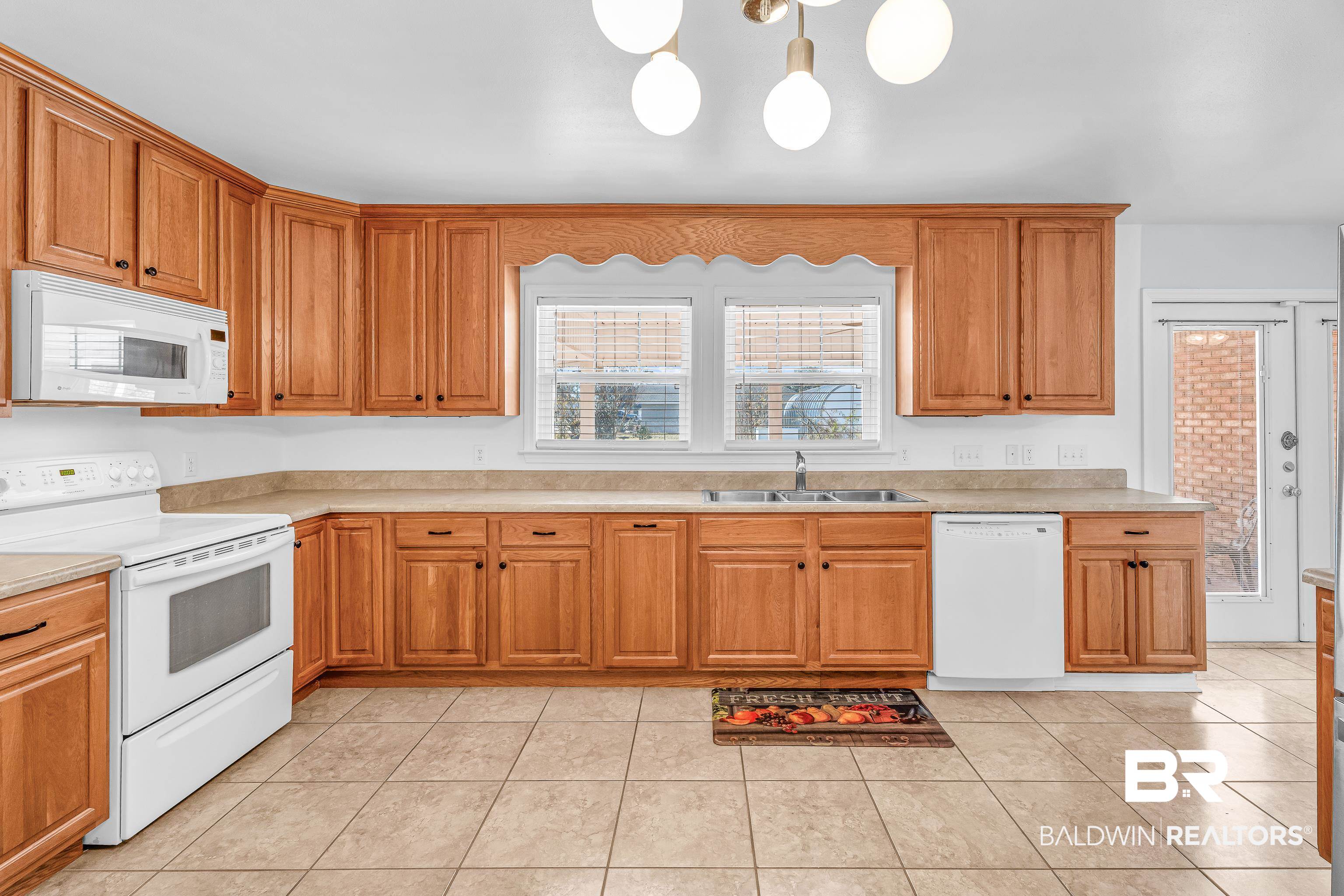22095 8th Street Silverhill, AL 36576 - Photo 21 of 42 Kitchen featuring white appliances, light countertops, wood finish cabinetry, light tile patterned flooring, and suspended lighting