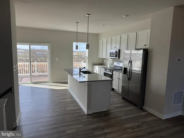 a kitchen with stainless steel appliances granite countertop a refrigerator a sink dishwasher a oven and a dining table with wooden floor