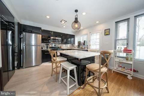 a kitchen with stainless steel appliances granite countertop a dining table chairs refrigerator and sink