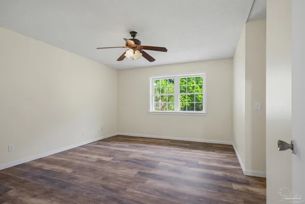 an empty room with wooden floor ceiling fan and windows