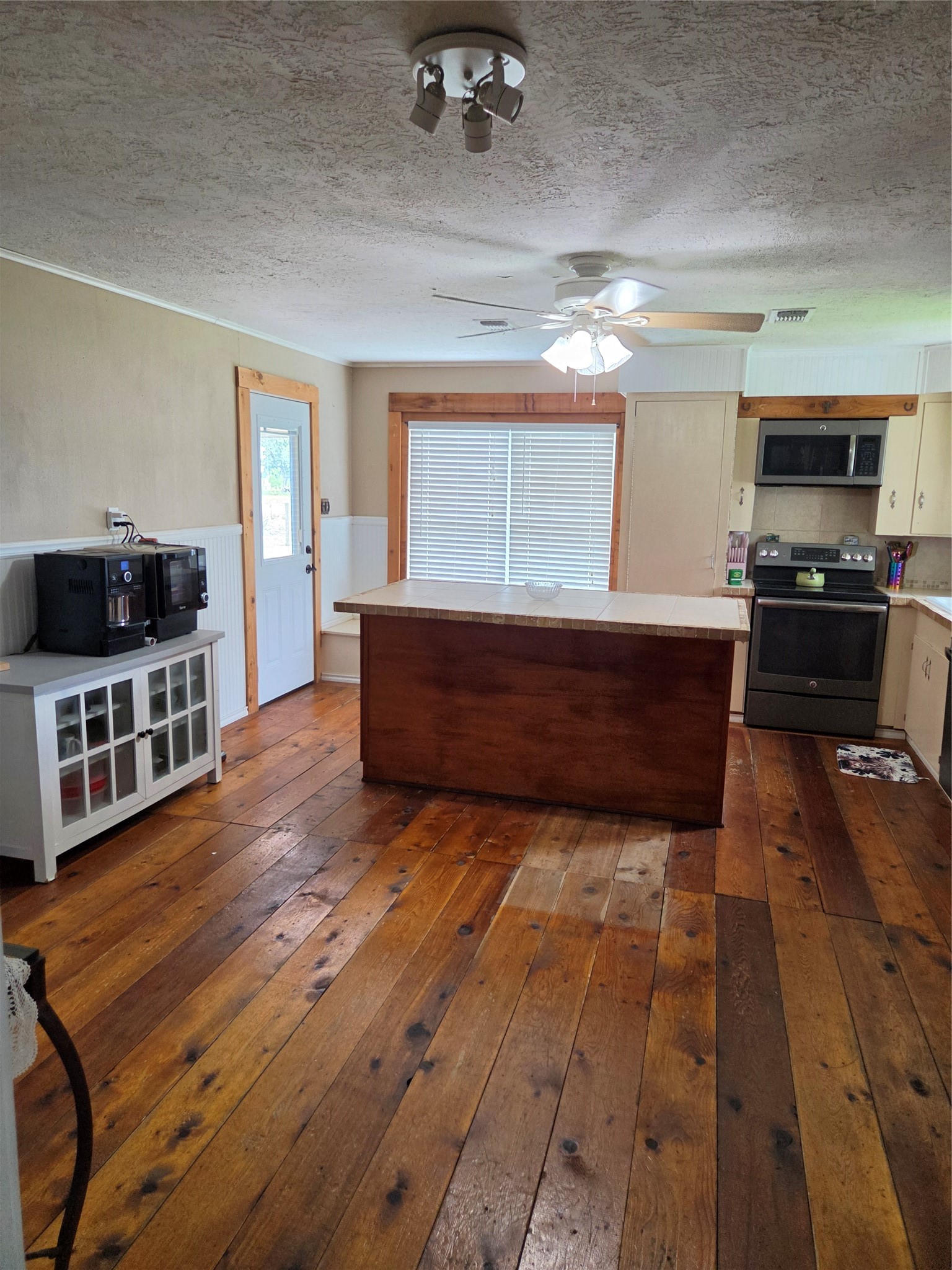 4910 FM 3012 Road Wharton, TX 77488 - Photo 14 of 21 This kitchen features rustic wooden flooring, a central island, and modern appliances. It has a ceiling fan, ample natural light from a large window with blinds, and a side door adds convenience.