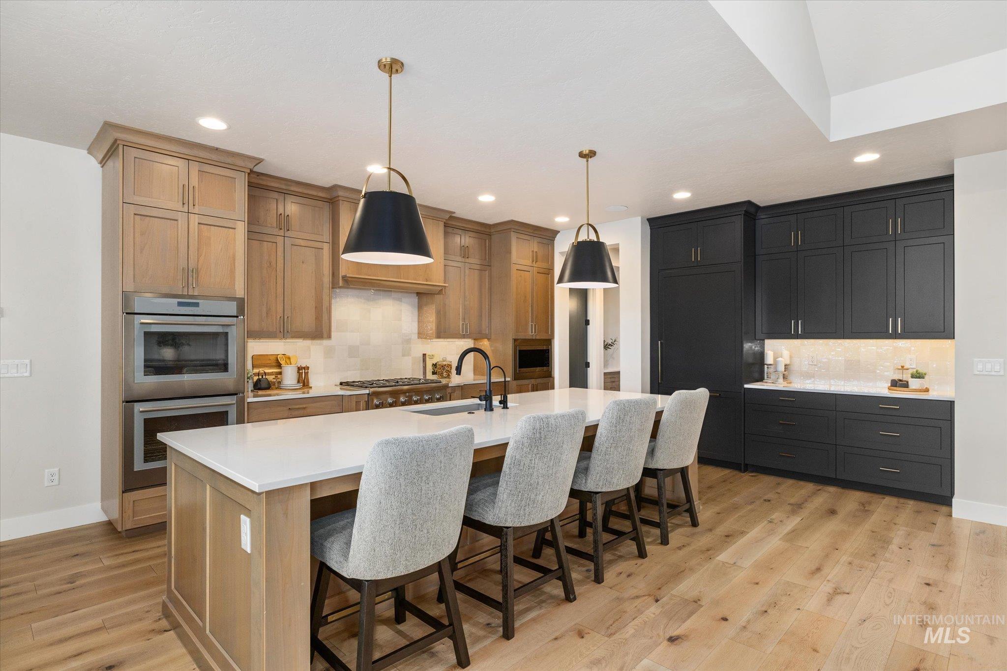 14857 Elk Spg Street Caldwell, ID 83607 - Photo 11 of 40 Kitchen featuring stainless steel appliances, light wood-type flooring, a kitchen bar, decorative light fixtures, and decorative backsplash