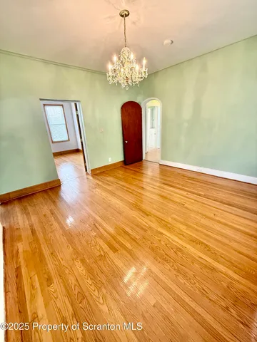 a view of an empty room with chandelier and wooden floor