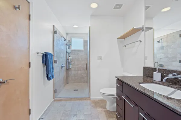 a bathroom with a granite countertop sink a toilet a mirror and shower