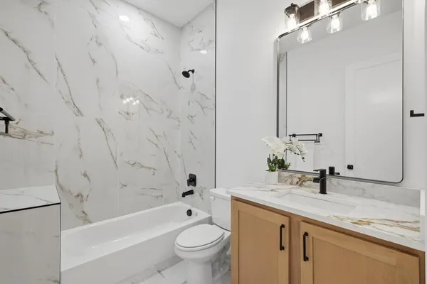 a bathroom with a granite countertop sink a toilet a mirror a bathtub and shower
