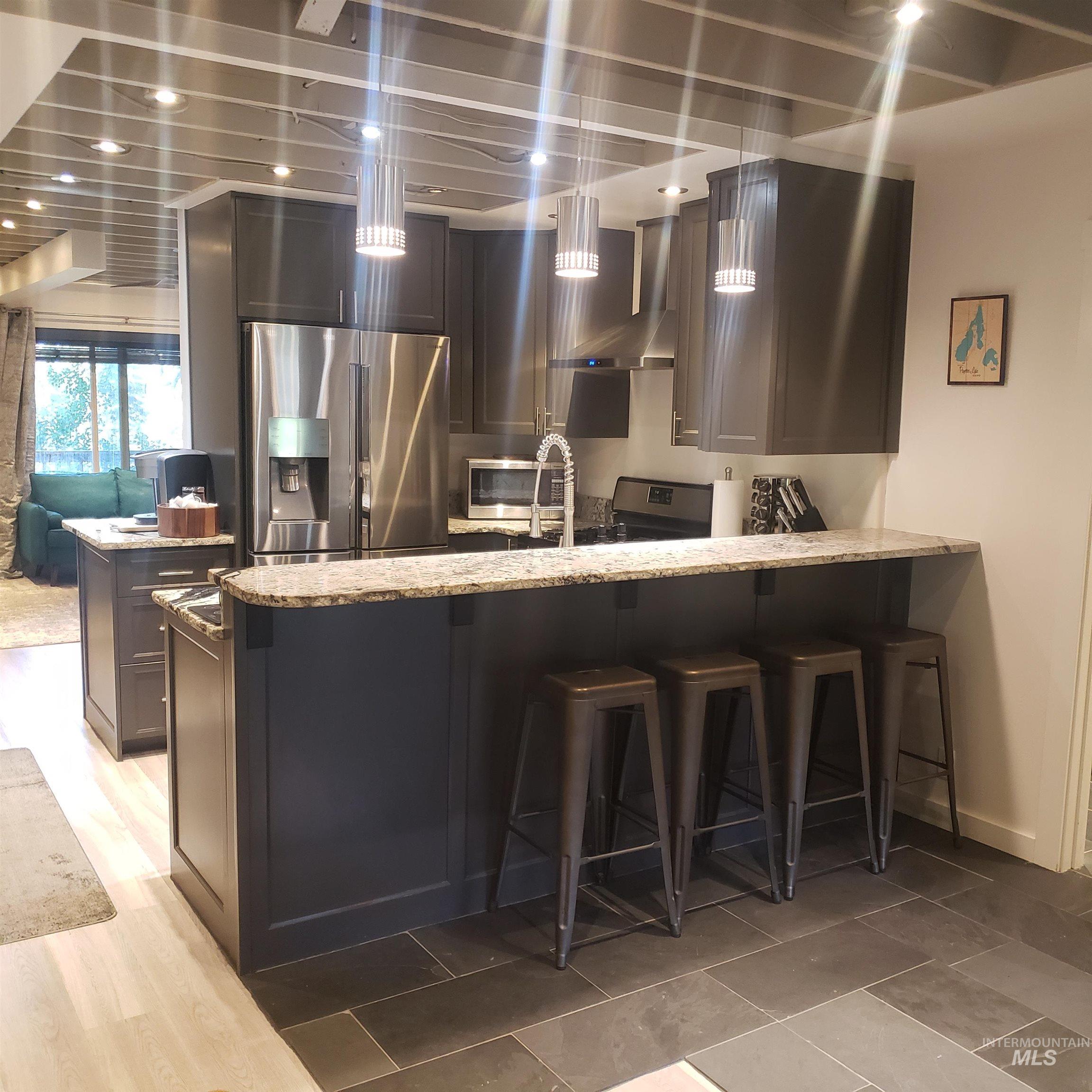1098 Crescent Rim Drive McCall, ID 83638 - Photo 4 of 42 Kitchen featuring a breakfast bar, stainless steel appliances, light stone countertops, decorative light fixtures, and wall chimney range hood
