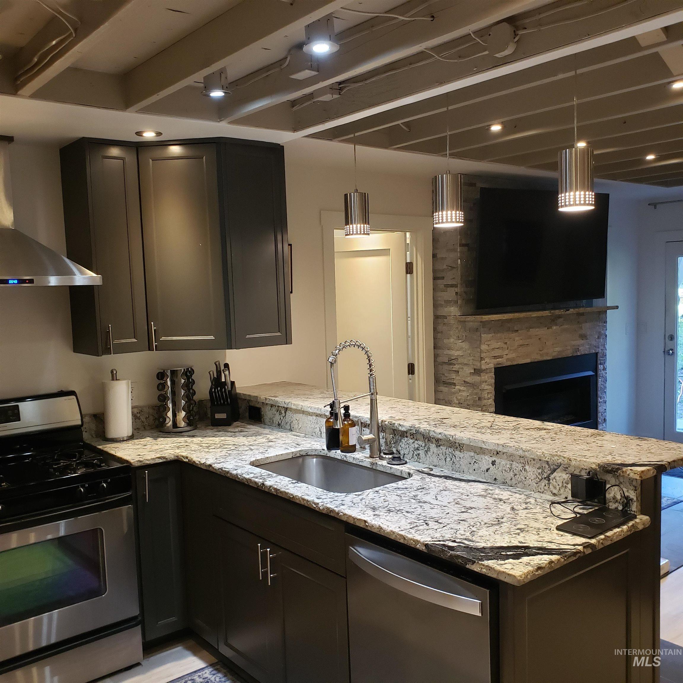 1098 Crescent Rim Drive McCall, ID 83638 - Photo 7 of 42 Kitchen featuring stainless steel appliances, pendant lighting, light stone counters, wall chimney range hood, and a peninsula