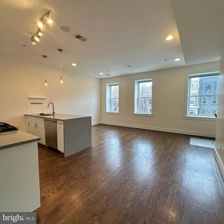 a view of an empty room and kitchen with wooden floor