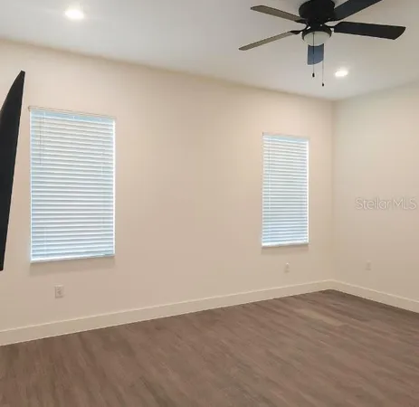 an empty room with wooden floor fan and windows