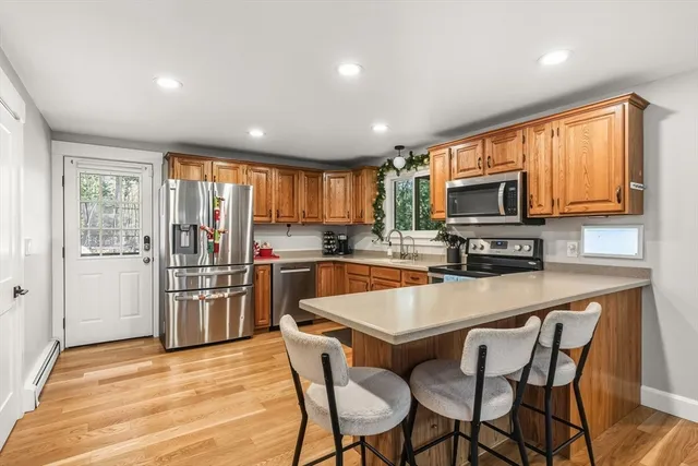 a kitchen with stainless steel appliances a microwave a stove a refrigerator a sink dishwasher a dining table and chairs with wooden floor