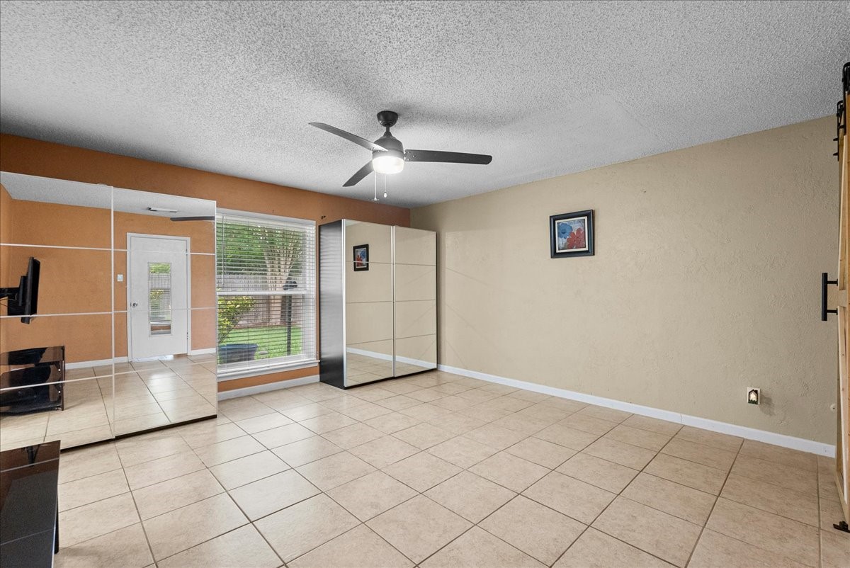 883 Silverpines Road Houston, TX 77062 - Photo 18 of 38 Primary bedroom features tiled flooring, a ceiling fan, and large mirrors that enhance the sense of space. A window and glass door provide ample natural light, with views of the outdoor area. Neutral wall colors and simple decor offer a versatile setting.