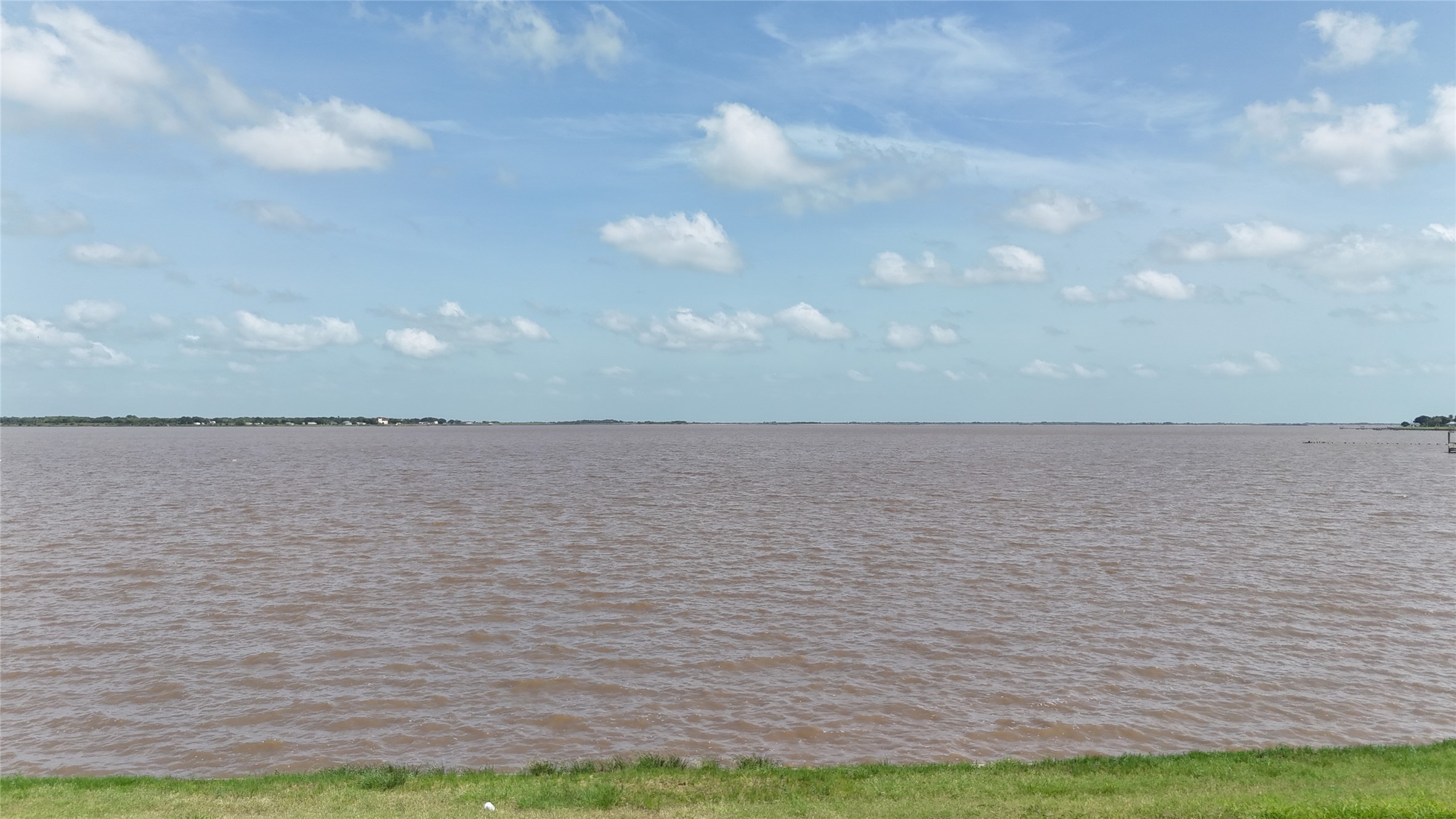 305 Bayshore Road Palacios, TX 77465 - Photo 20 of 25 A tranquil expanse of water stretches towards a distant tree-lined horizon under a bright sky.