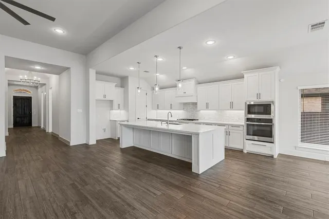 a large kitchen with a center island wooden floor and stainless steel appliances