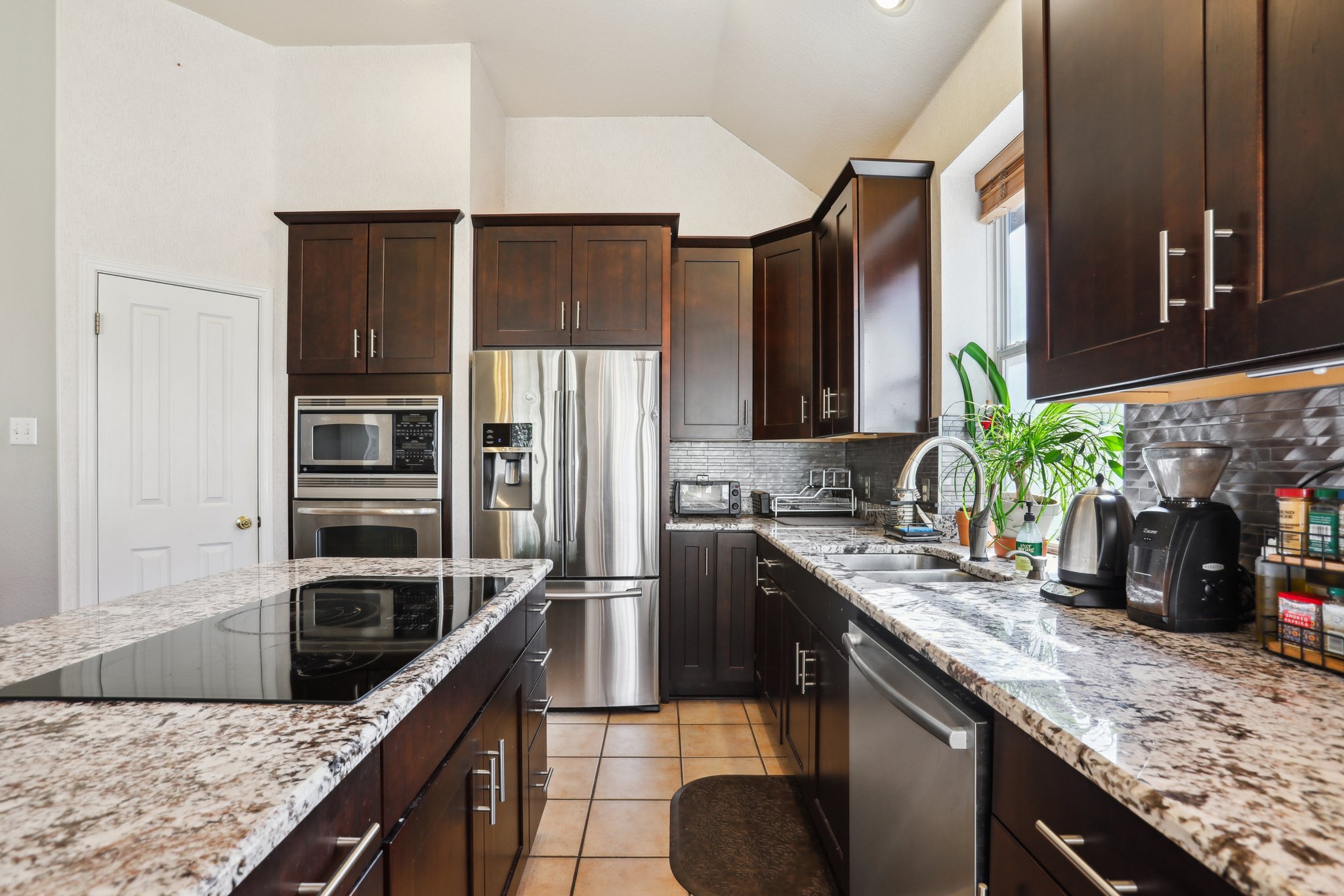 13541 Anarosa Loop Austin, TX 78727 - Photo 8 of 27 Kitchen featuring dark wood cabinetry, stainless steel appliances, a built-in oven and microwave, granite countertops, and a tile backsplash