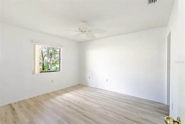an empty room with wooden floor ceiling fan and windows