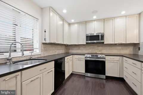 a kitchen with stainless steel appliances granite countertop a sink a stove a white cabinets and a window