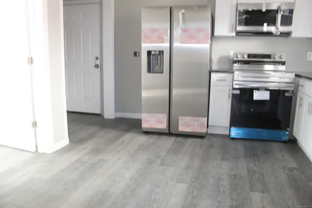 a view of kitchen with stainless steel appliances wooden floor and living room