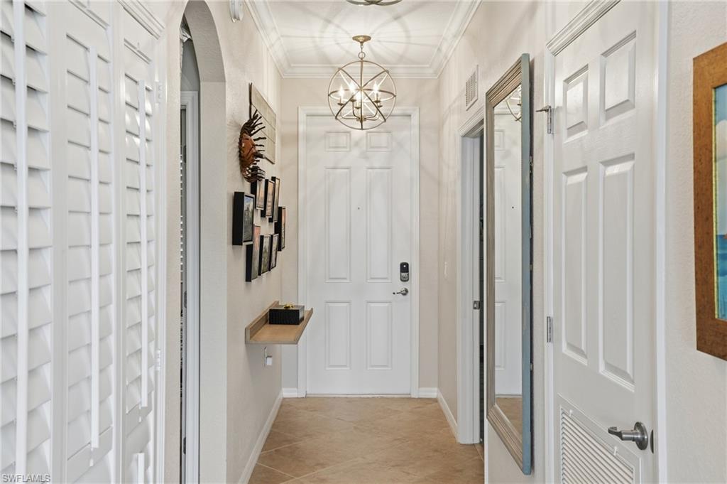 Corridor featuring arched walkways, ornamental molding, a chandelier, and light tile patterned floors