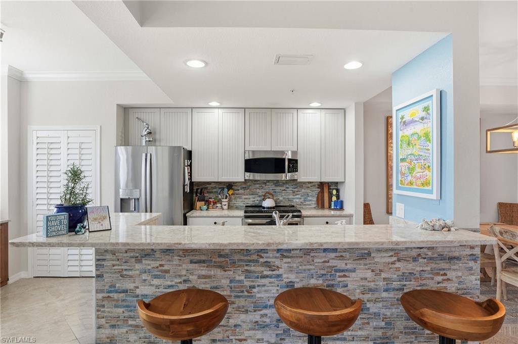 9715 Acqua Court, Unit 113 Naples, FL 34113 - Photo 3 of 31 Kitchen with light stone countertops, a kitchen breakfast bar, stainless steel appliances, tasteful backsplash, and recessed lighting