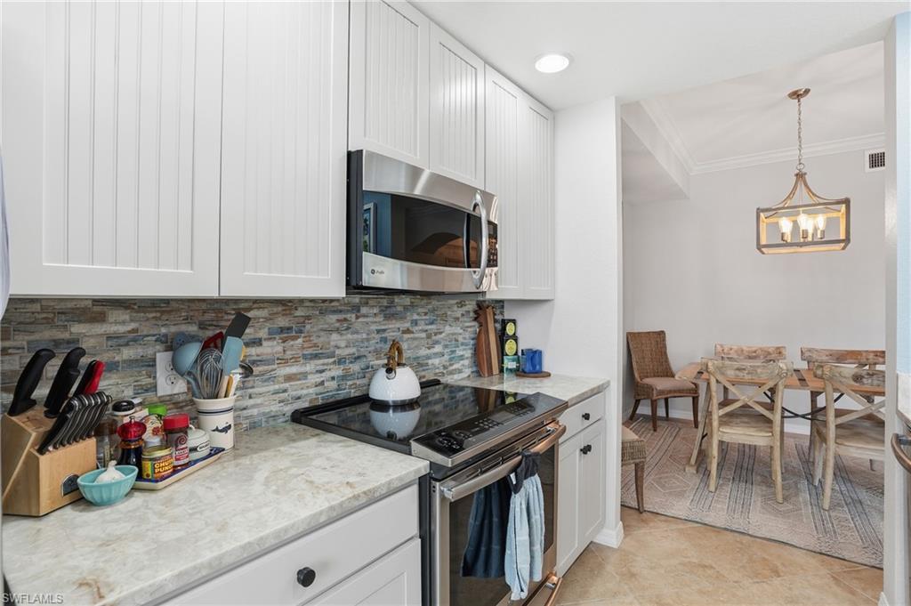 9715 Acqua Court, Unit 113 Naples, FL 34113 - Photo 7 of 31 Kitchen featuring stainless steel appliances, white cabinets, pendant lighting, ornamental molding, and light stone counters