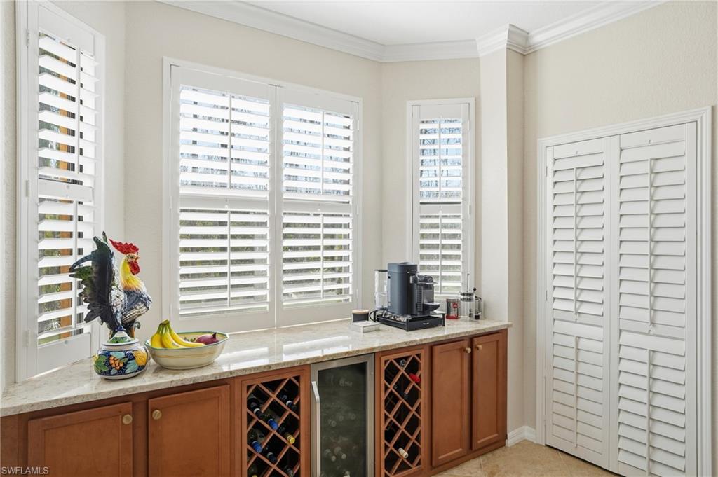 9715 Acqua Court, Unit 113 Naples, FL 34113 - Photo 8 of 31 Bar with light stone counters, wine cooler, ornamental molding, and wood finish cabinets