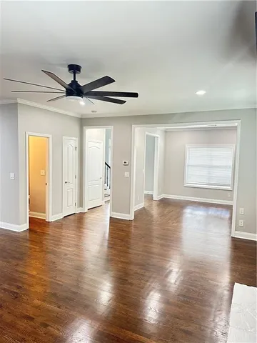 a view of an empty room with wooden floor and a ceiling fan