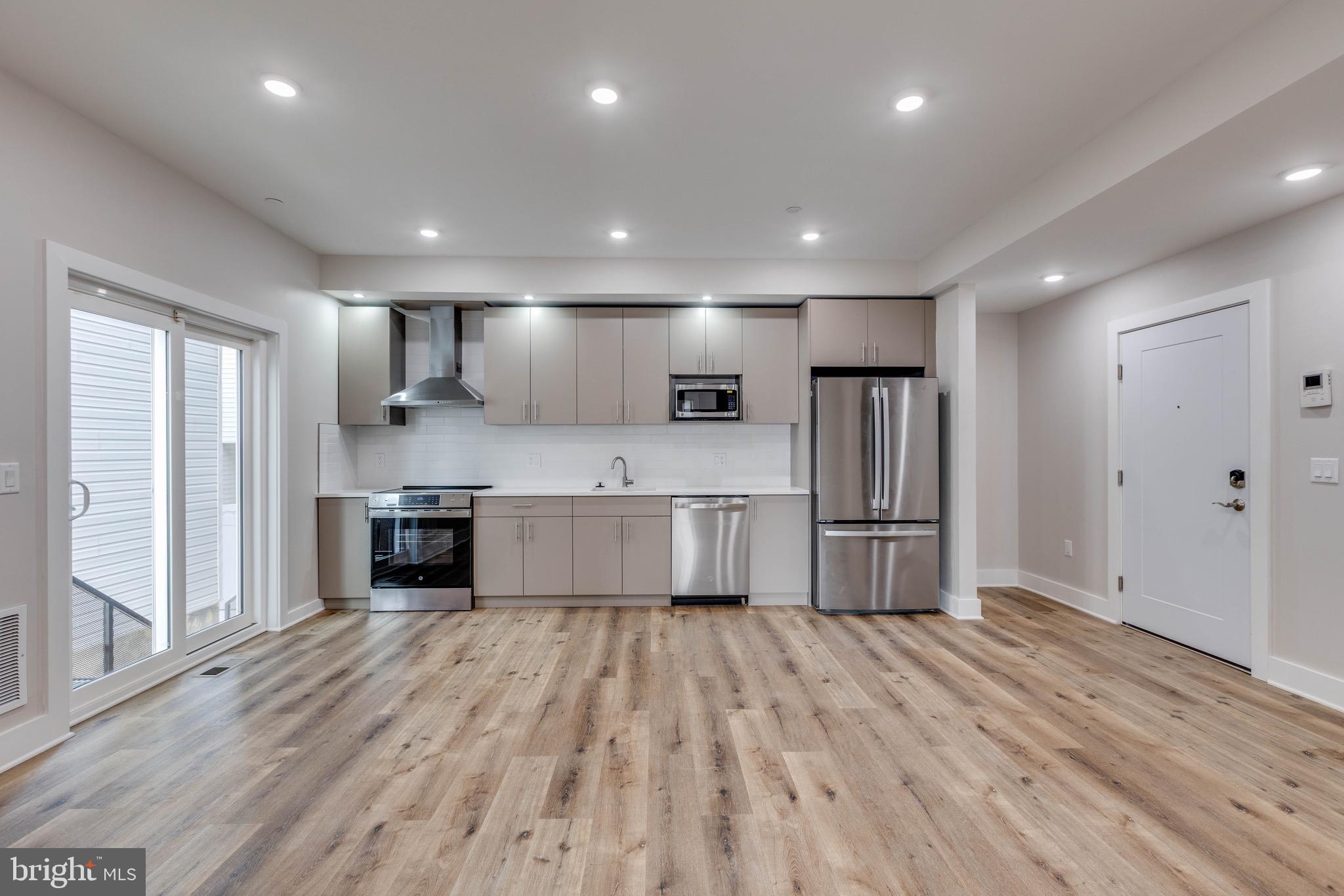 a large kitchen with stainless steel appliances wooden floor a large window and a sink