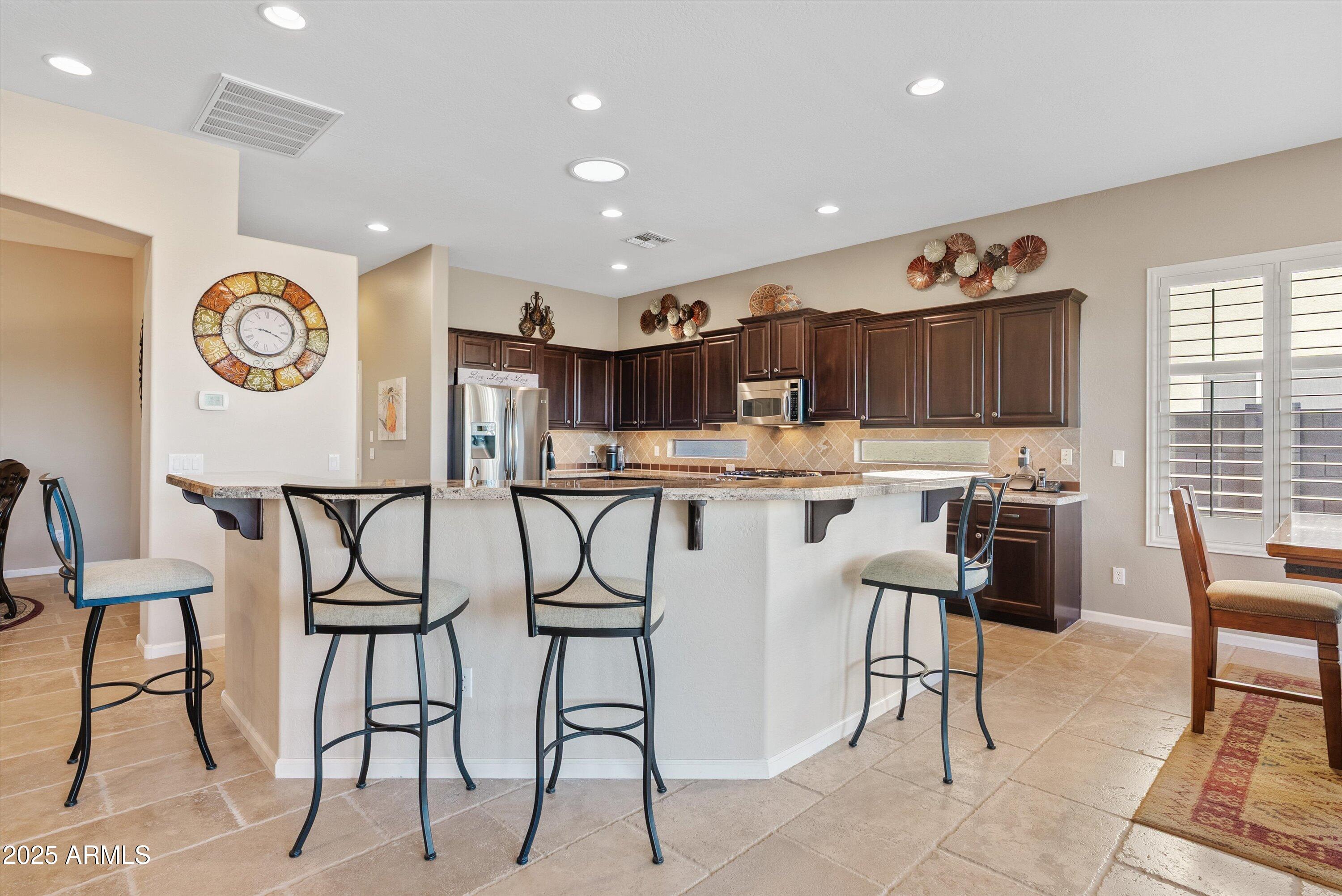 6805 Rachael Way Gilbert, AZ 85298 - Photo 9 of 50 a kitchen with stainless steel appliances kitchen island granite countertop a table chairs and a refrigerator