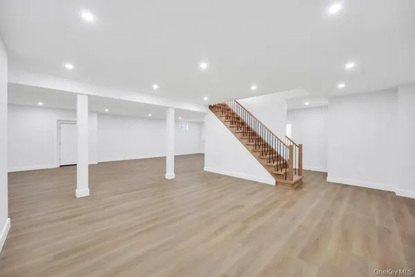 a view of an empty room with wooden floor stairs and a way to kitchen
