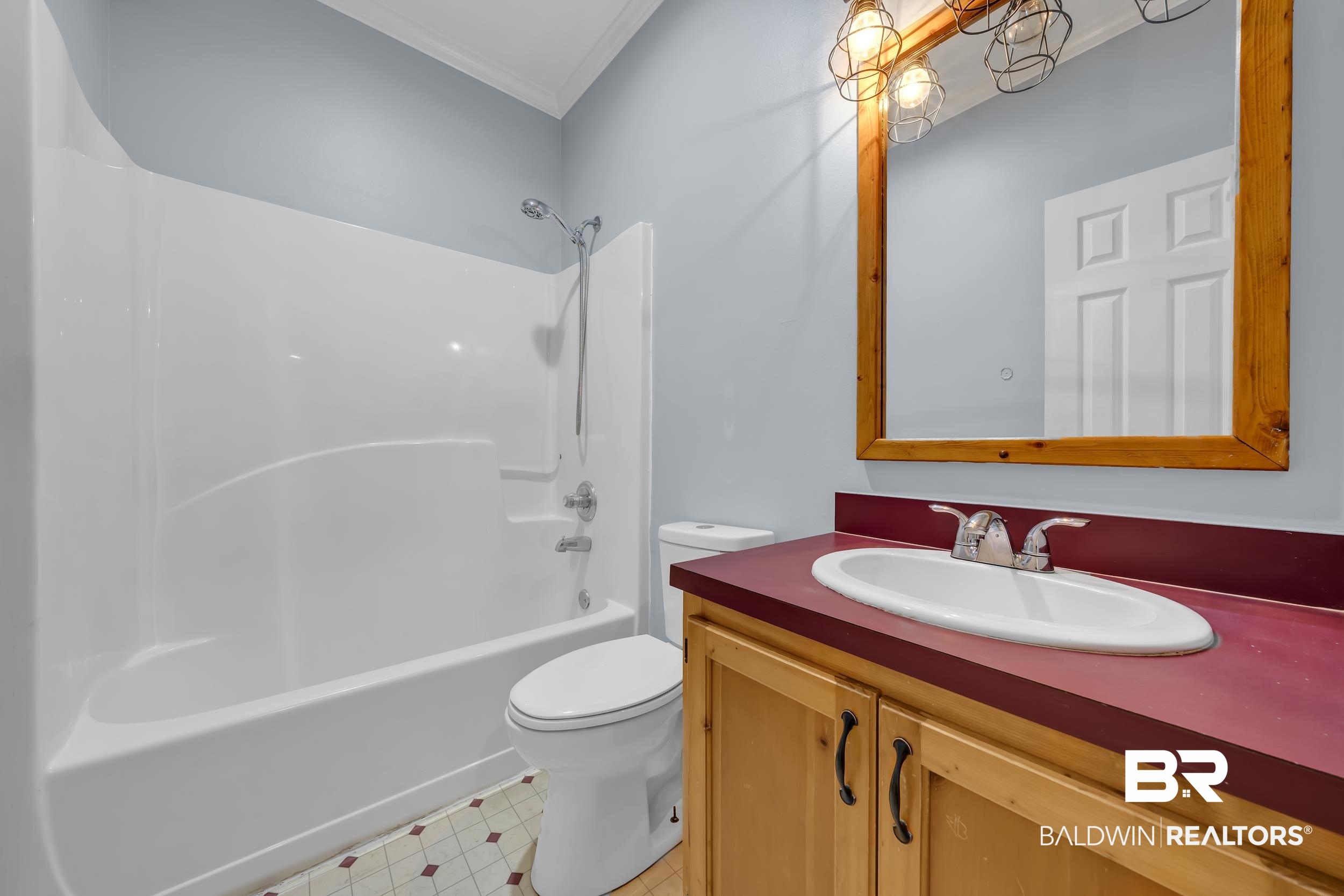 14960 Howells Ferry Road Wilmer, AL 36587 - Photo 20 of 22 Bathroom featuring a single-piece tub and shower unit, a wood-finish vanity with a red countertop, and a framed mirror with an industrial-style light fixture