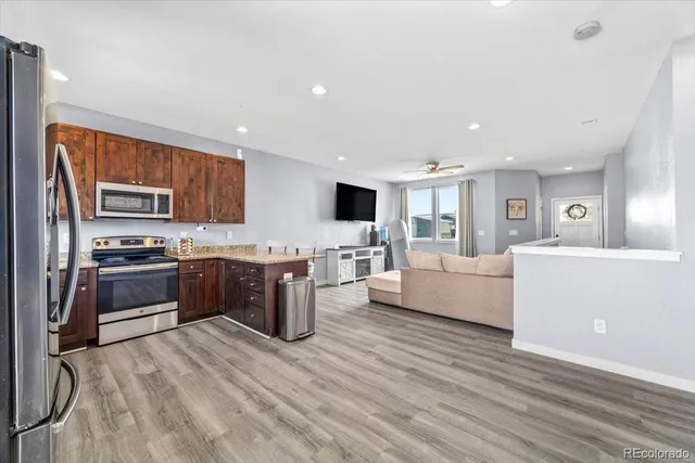 a large white kitchen with stainless steel appliances kitchen island granite countertop a stove a sink dishwasher a refrigerator and white cabinets with wooden floor