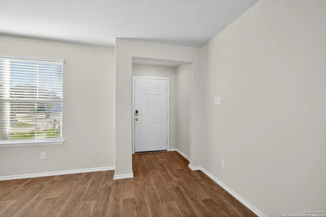 a view of an empty room with wooden floor and a window