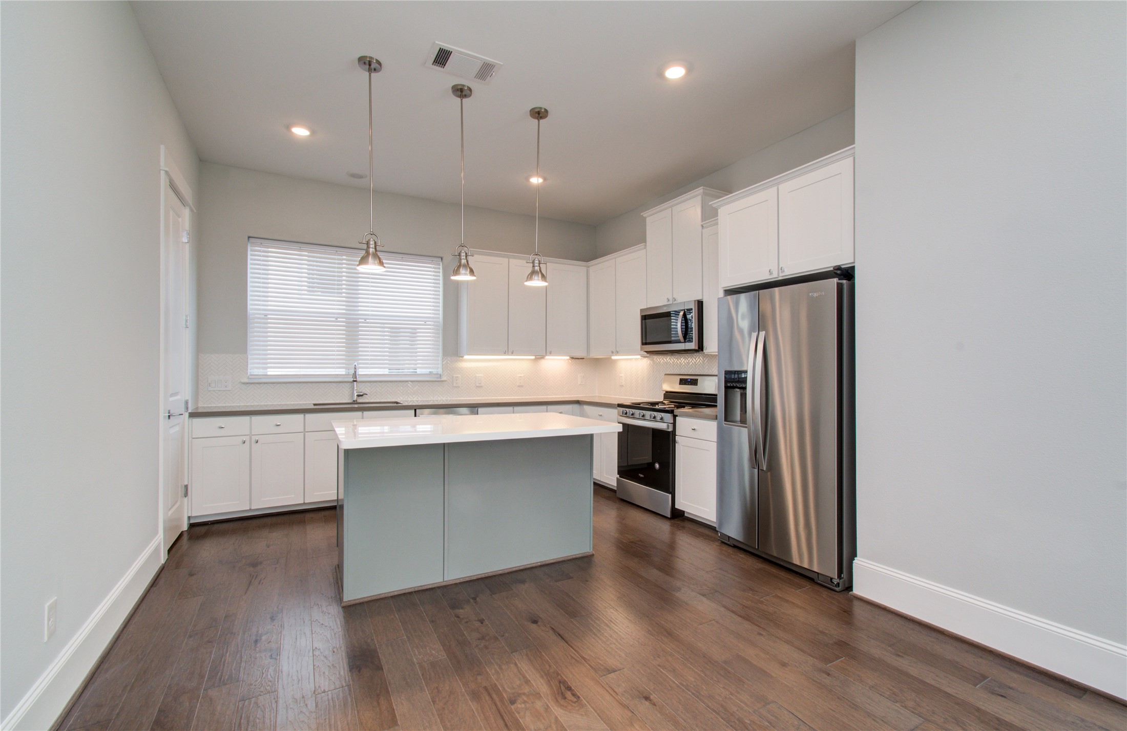 1262 North Post Oak Road, Unit A Houston, TX 77055 - Photo 18 of 50 The modern kitchen is equipped with stainless steel appliances, white cabinetry, and a contrasting sage green island with white countertops. Trio pendant lights hang above the island, offering functional task lighting over the workspace.