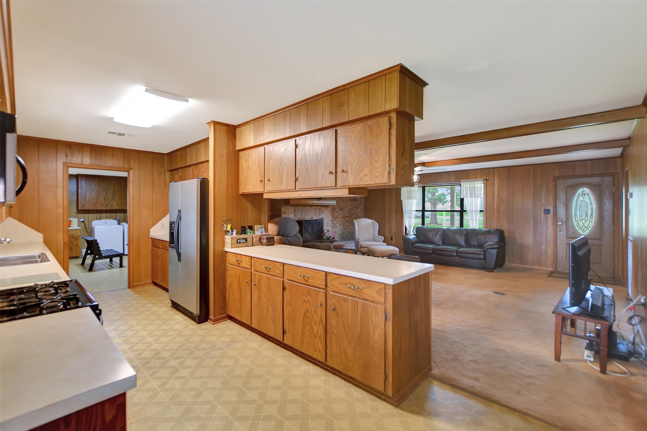 341 South S Loop Bellville, TX 77418 - Photo 12 of 33 This cozy kitchen and living area with wood paneling and cabinetry, a stainless steel fridge, and an open layout that connects to a living room with large windows and a front door.
