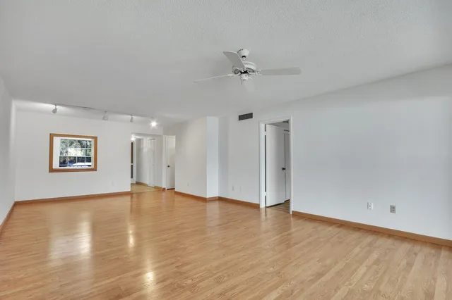 an empty room with wooden floor ceiling fan and windows