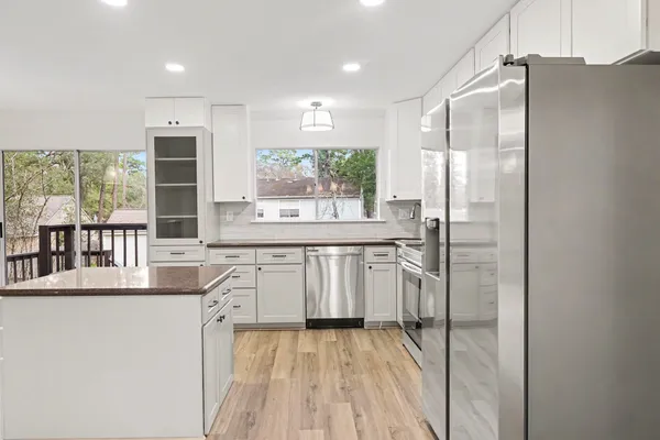 a kitchen with stainless steel appliances granite countertop a refrigerator a sink a stove and white cabinets with wooden floor