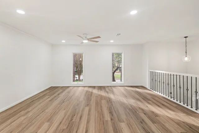 an empty room with wooden floor fan and windows