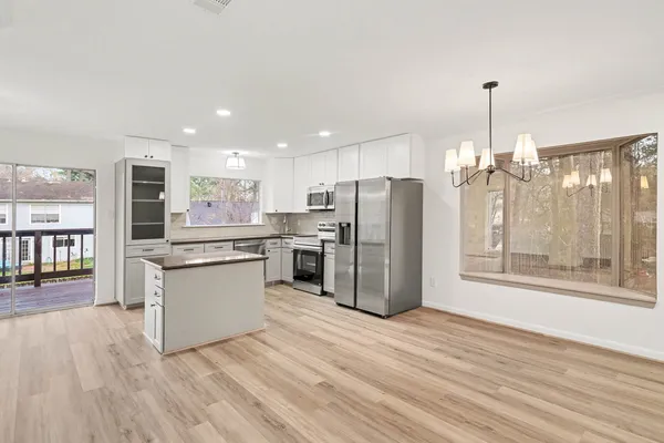 a kitchen with stainless steel appliances kitchen island granite countertop a refrigerator a sink dishwasher a stove and a dining table with wooden floor