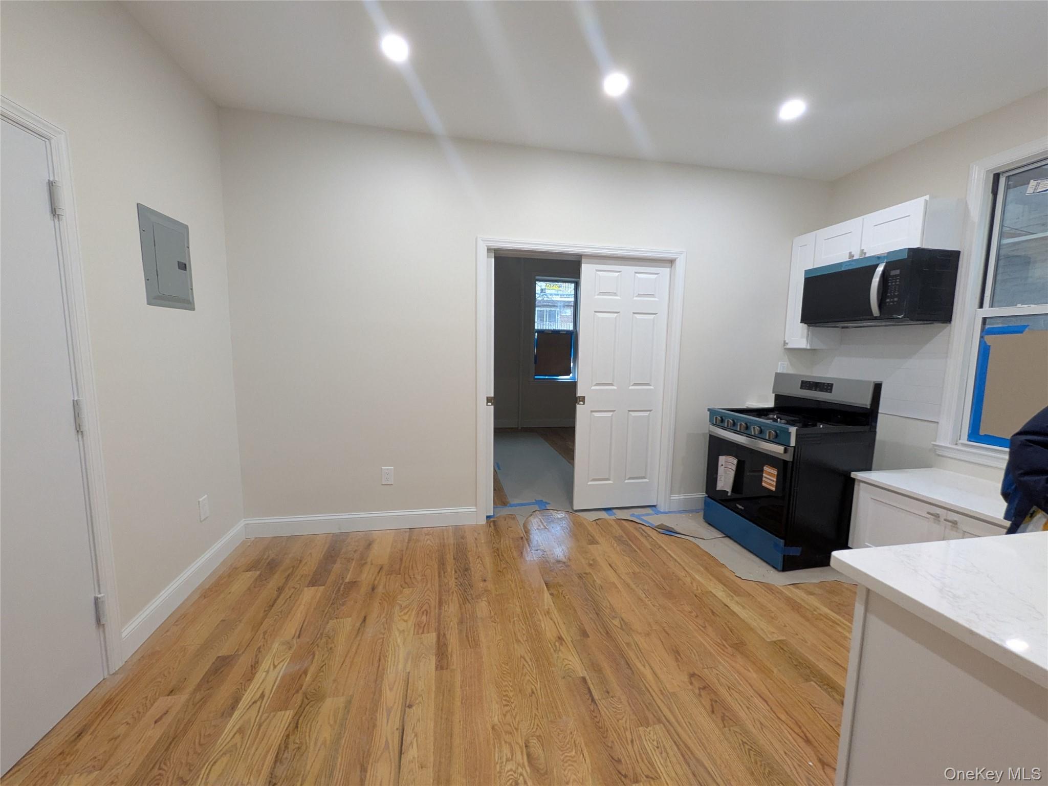 Kitchen with white cabinets, gas range oven, light wood-style flooring, black microwave, and electric panel