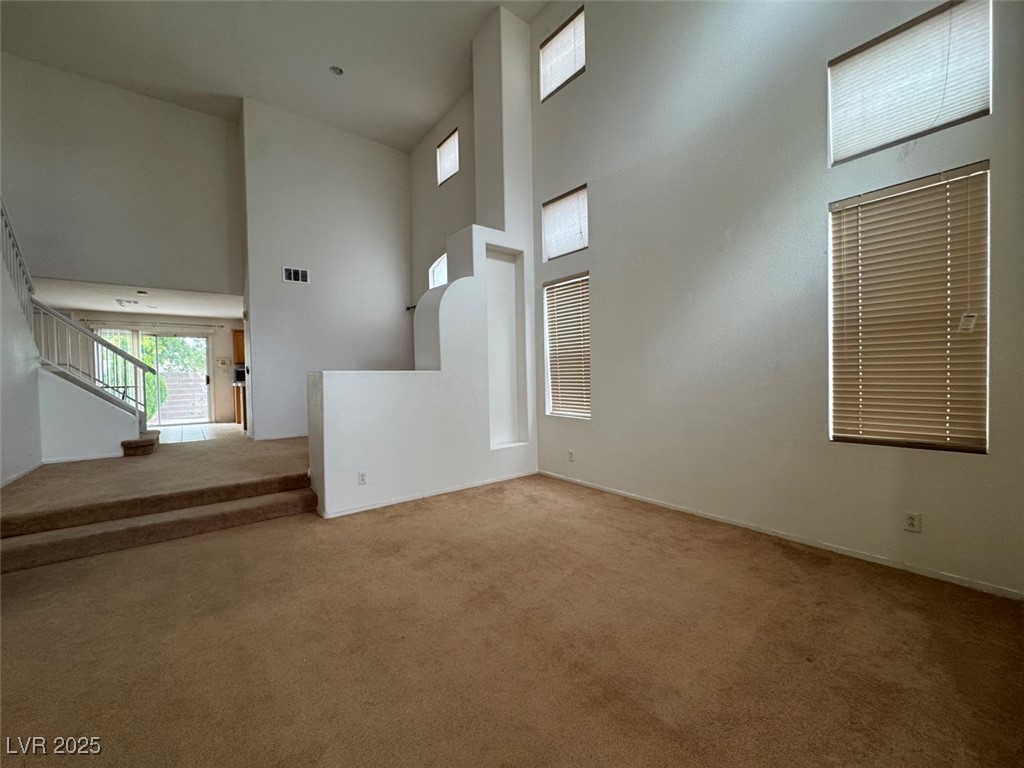 9915 Ridge Hill Avenue Las Vegas, NV 89147 - Photo 3 of 17 Unfurnished living room with a towering ceiling, light carpet, and stairway