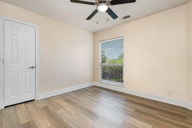 an empty room with wooden floor chandelier fan and windows
