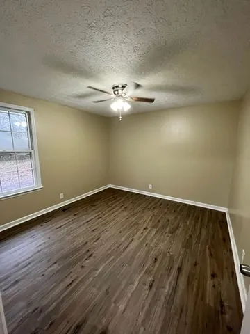 an empty room with wooden floor fan and windows