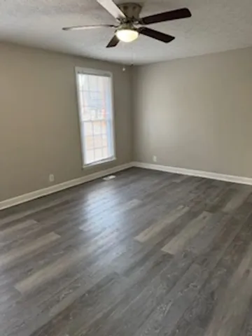 an empty room with wooden floor fan and windows