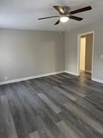 a view of an empty room with wooden floor and a ceiling fan