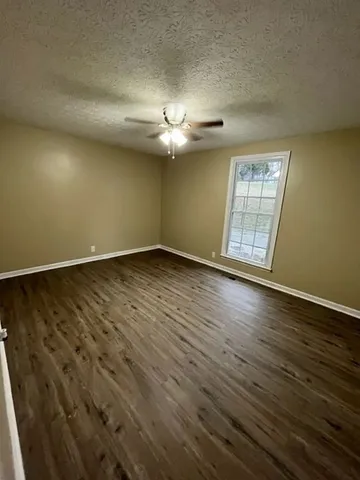 an empty room with wooden floor chandelier fan and windows