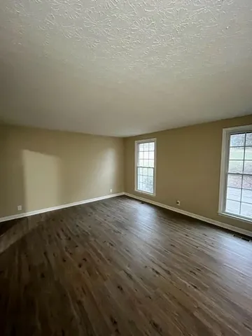 a view of an empty room with wooden floor and window